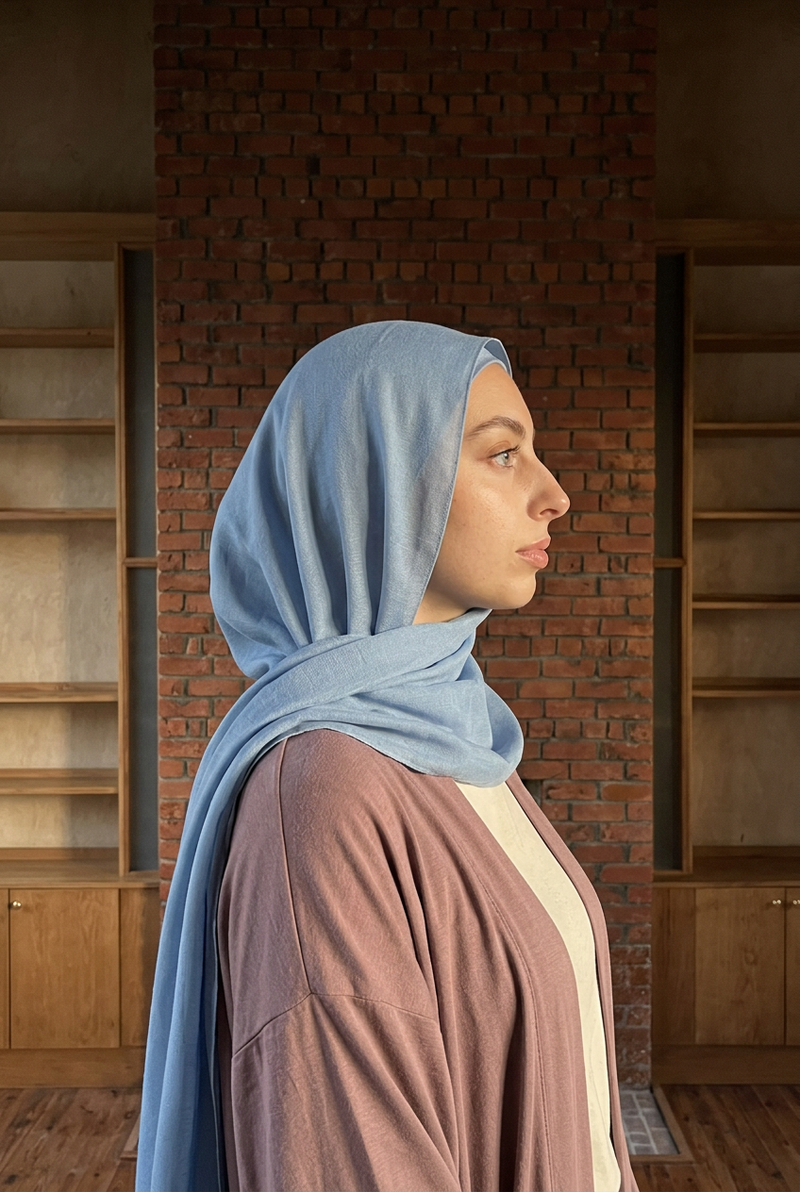 Ensemble hijab et bonnet bleu vu de profil devant une cheminée en brique