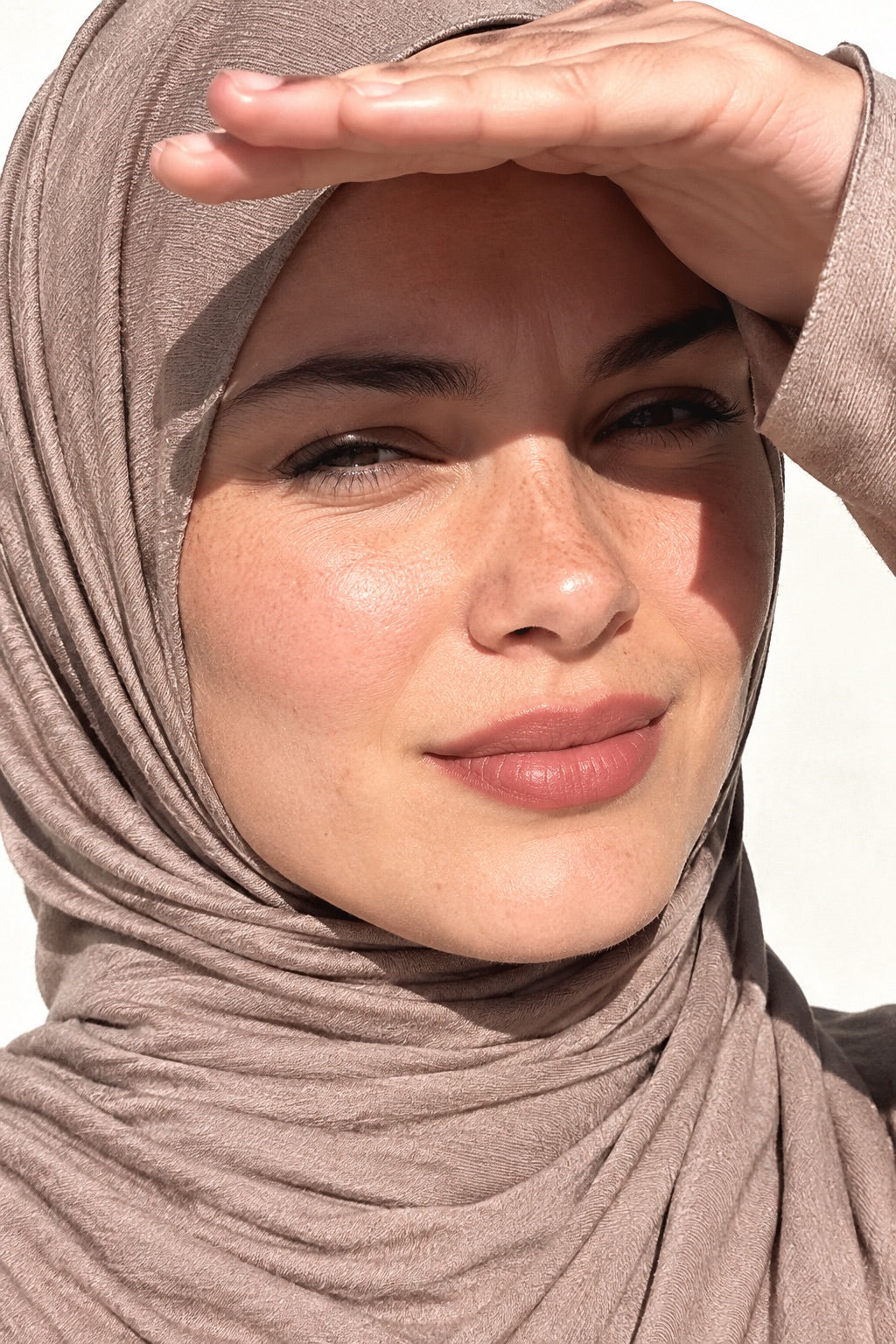 Femme en hijab jersey court taupe, la main en visière au soleil