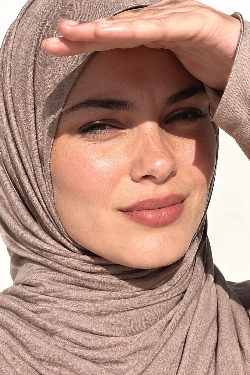 Femme en hijab jersey court taupe, la main en visière au soleil