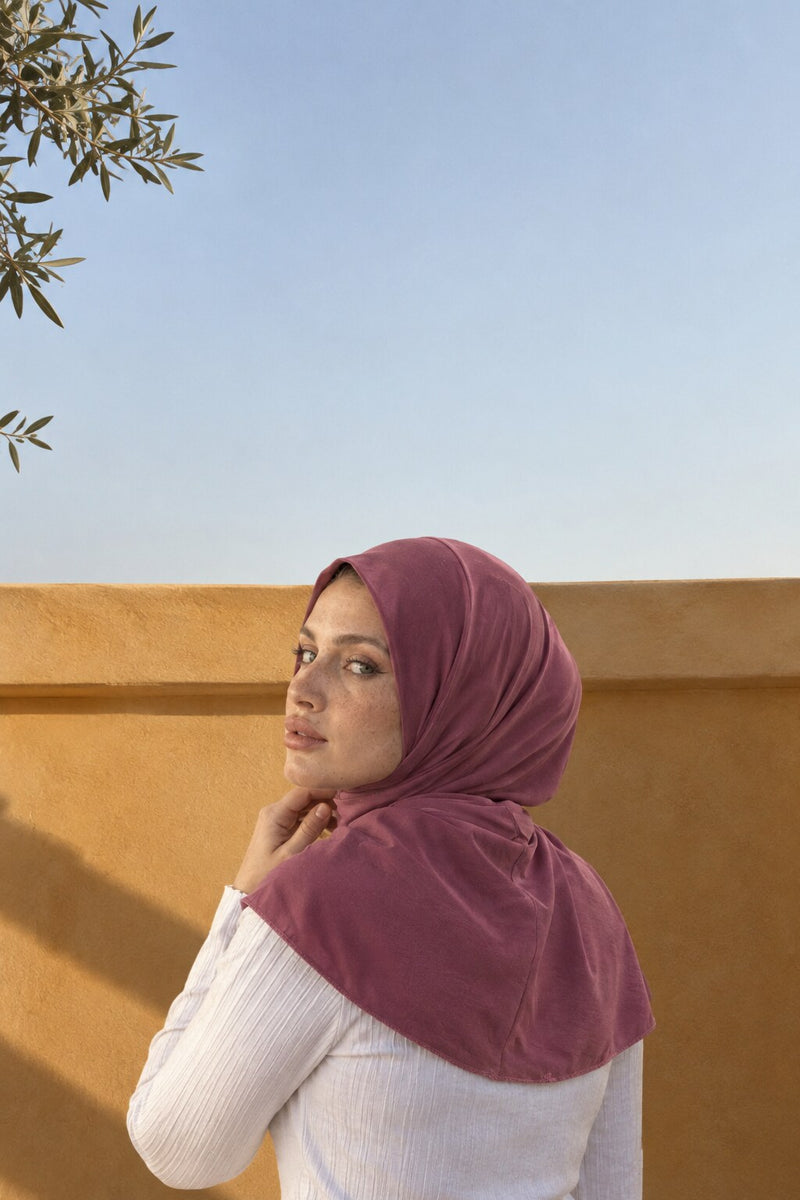 Femme portant le hijab à pression, vue de dos et tournée vers l'objectif, devant un mur ocre
