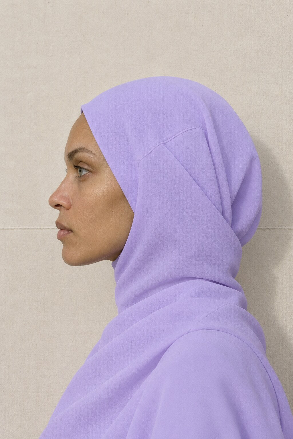 Hijab mousseline lilas noué, vu de profil devant une toile écrue