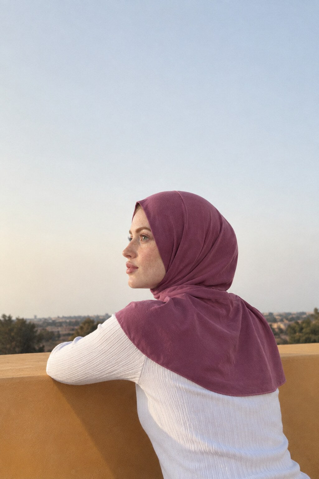 Femme en hijab à pression accoudée à un muret, face au soir